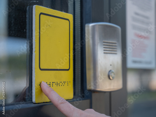 A blind woman reads the braille sign next to a call button.