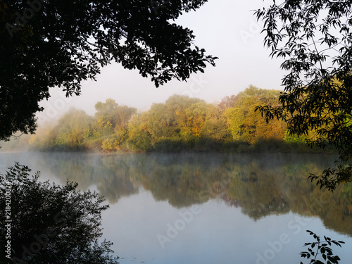 Autumn misty dawn, morning fog over the river. The first yellow leaves on the trees.