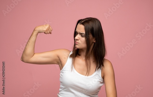 Obraz na plátně Young woman flexing biceps, showing determination and strength on a pink backgro