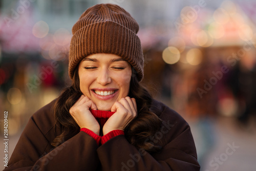 Fotografie Cheerful woman smiling and holding sweater collar at festive Christmas fair