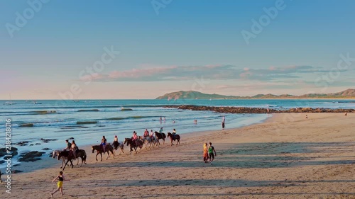 Aerial drone shot of tourists horseback riding on the beach at sunset