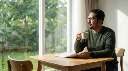 Man drinking morning coffee at home table by window