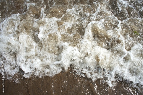 Fotografie Close up of frothy white sea foam breaking on wet shore sand