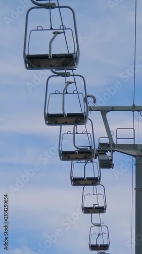 Vertical video: empty chairlifts at the summit of Mount Babadag, moving against blue sky with clouds in Mugla, Turkey. Mountain transport, tourism and scenic landscape concept