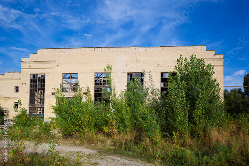 Abandoned ruined overgrown by plants industrial building waiting for demolition. Territory of abandoned industrial area of Voronezh excavator factory