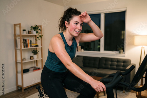 Side View of Fit Young Woman Holding Towel and Cheering Victory on Stationary Bike, Daily Indoor Fitness Routine