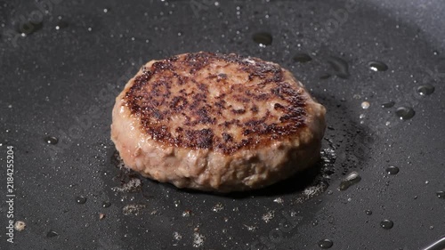 Grilled hamburger steak patty with seared crust cooking on a black griddle, camera zooms in and pans across the surface