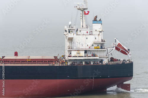 Foto Large bulk carrier underway on a tranquil sea during an early misty morning, creating an atmospheric maritime scene with the ship surrounded by light haze
