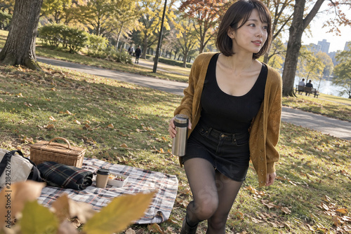 Obraz na płótnie 秋の公園のピクニックで魔法瓶を持ち立ち上がる茶色カーディガンの女性
