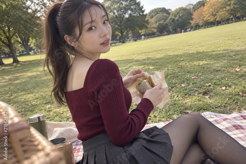Obraz na płótnie 秋の公園のピクニックでサンドイッチを持ち振り返るバーガンディ色トップスの女性