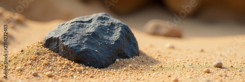 Rough dark stone partially buried in light brown sand , stone, heavy