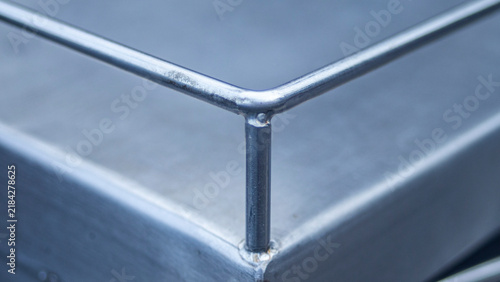 Close up of stainless steel railing weld joint on a metallic surface.A detailed close-up shot focusing on the weld joint corner of a stainless steel or iron protective railing. 