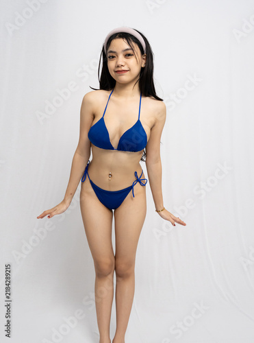 Fotografie Young Asian Woman In Blue Bikini Standing In Front Of White Background With Stud