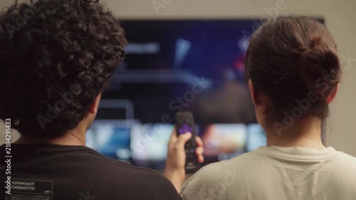 Diverse couple using remote to navigate streaming platform on smart television at night