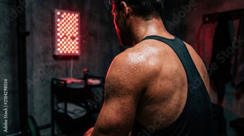 Muscular Man’s Back Sweated Under Red LED Panel Light in Dark Gym Setting showing Fitness Training Atmosphere