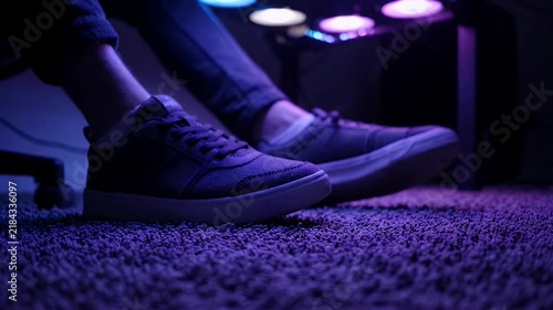 Gamer feet in sneakers sitting on carpet in neon blue gaming room lighting