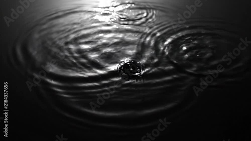 A single ripple spreads across the dark and calm water surface