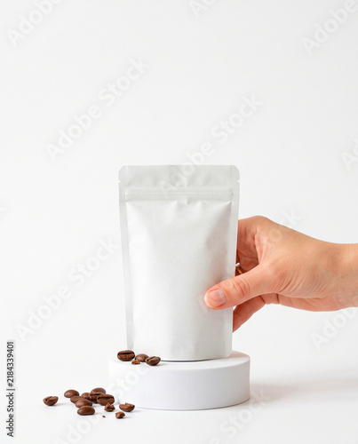 Hand Holding Blank White Coffee Pouch Mockup with Coffee Beans on Podium
