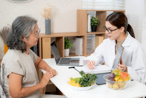 Asian woman nutritionist showing AI BMI calculator on tablet and explaining to senior patient, doctor using digital health technology for medical diagnosis, wellness planning and weight control.