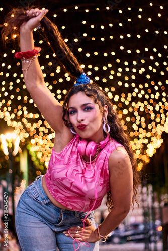 Foto Beautiful, made-up, cheerful woman, straightening her hair, charismatic, dressed in colorful clothes, against a backdrop of lights, outdoors