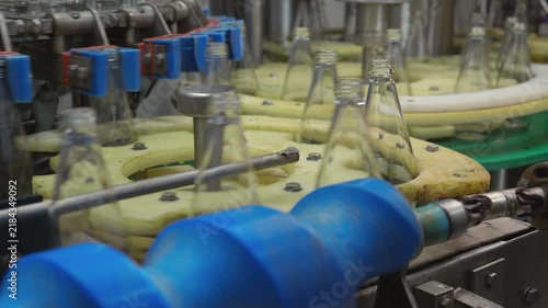 Empty glass bottles moving along circular automated conveyor system inside industrial juice production plant facility, manufacturing process and high technology automation, supply chain.