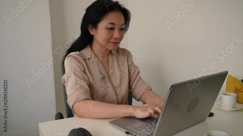 Footage of Asian businesswoman typing on a laptop and using a wireless mouse at an office desk. Professional workplace scene illustrating business, technology, productivity and remote work.