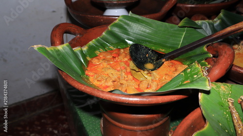 Spicy indonesian gravy curry beautifully presented in a rustic earthenware pottery bowl lined with vibrant green banana leaf for authentic heritage dining.