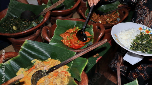 Traditional javanese food buffet featuring assorted spicy coconut milk curries served inside rustic clay pots lined with organic fresh green banana leaves.