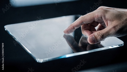 Close-up of human hand tapping tablet touchscreen on dark surface, finger pressing illuminated display, modern technology interaction, sleek minimalist setup, dim moody lighting