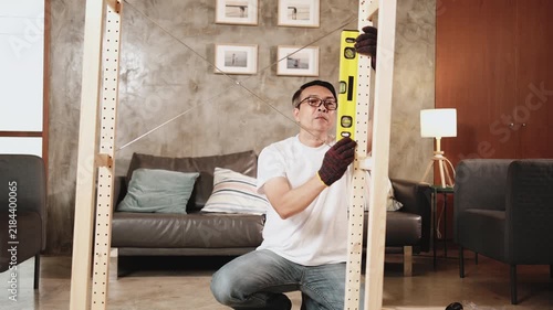 Asian mature man self-assembling wooden furniture with DIY tools, checking work precision with spirit level, home improvement, craft installation, hobby carpentry workshop, handyman active lifestyle.