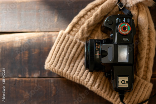 A camera and a wool hat on a rustic wooden table, ready for a trip or a camping trip in nature