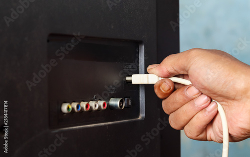 фотографія Close-up of a hand plugging a white HDMI cable into an HDMI port on the back of a television