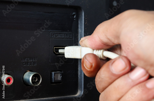 Obraz na plátně Close-up of a hand plugging a white HDMI cable into an HDMI port on the back of a television