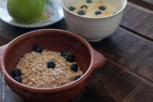 A small country-style clay bowl filled with oats and blueberries, ready for a healthy breakfast in a rustic kitchen setting