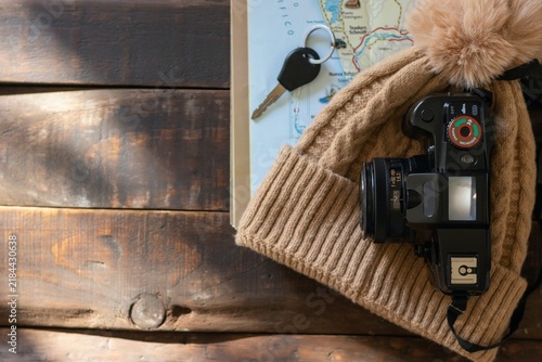 A bird's-eye view of a rustic wooden table with travel items on it: a map, a camera, and a wool hat