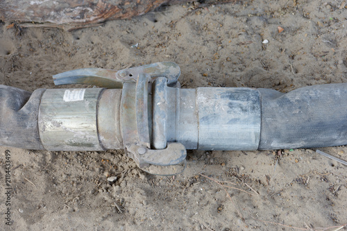 Rusty industrial hose coupling and rubber hose lying on ground, showing wear and heavy use at a construction or irrigation site, evoking maintenance, repair, and outdoor work.
