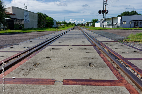 Low-angle photo of rusty train tracks stretching into the distance across gravel and wooden sleepers in a suburban St. Petersburg, FL green setting, suggesting travel, solitude, perspective, industria