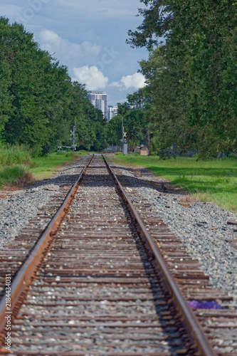 Low-angle photo of rusty train tracks stretching into the distance across gravel and wooden sleepers in a suburban St. Petersburg, FL green setting, suggesting travel, solitude, perspective, industria