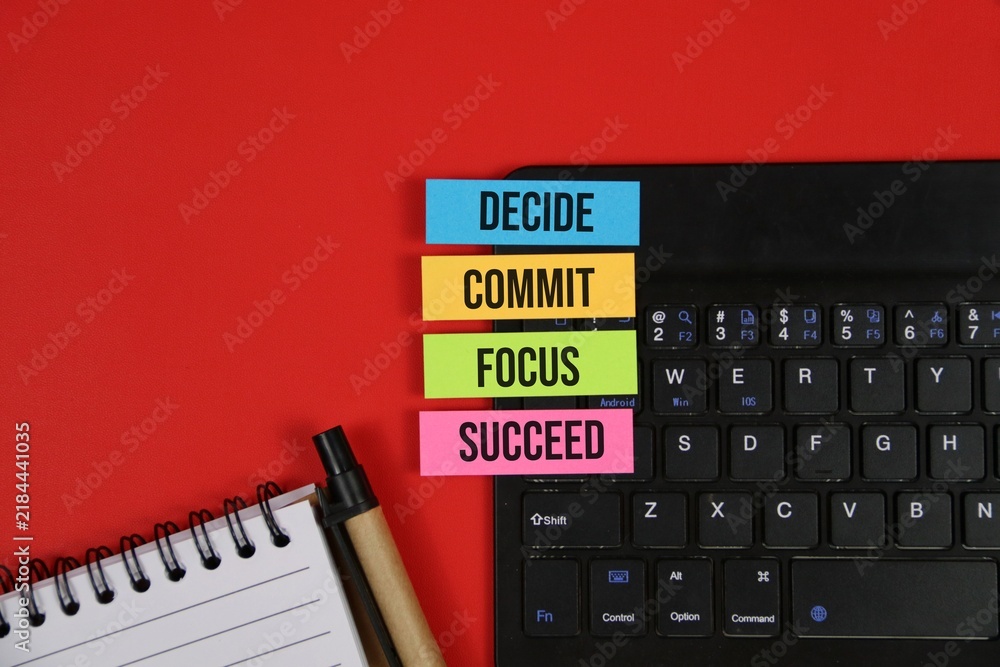 Obraz premium Business motivation concept with colorful sticky notes labeled decide, commit, focus, and succeed on a laptop beside a notebook and pen. with an red background.