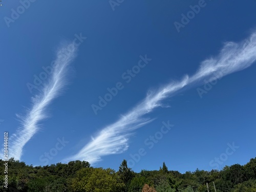 Wispy cirrus clouds in a deep blue sky above a green forested ridge