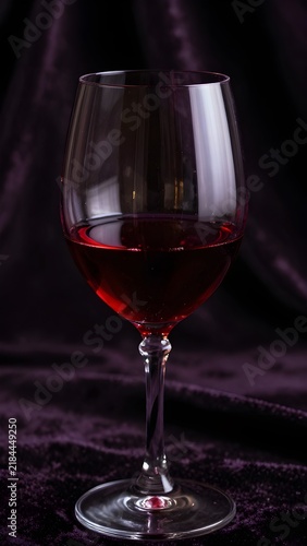 Glass of red wine on dark purple velvet fabric with dramatic light