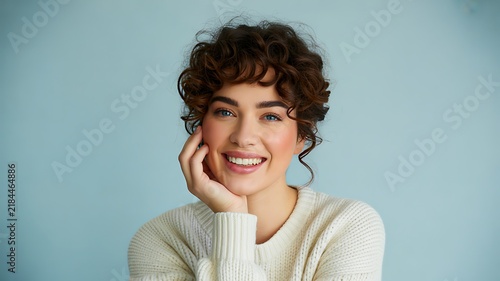 Smiling woman with curly hair posing against a soft blue background