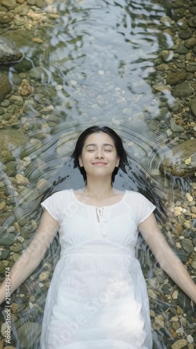Beautiful Young Woman Floating Peacefully in Shallow Clear Creek Water. Top view. Vertical video
