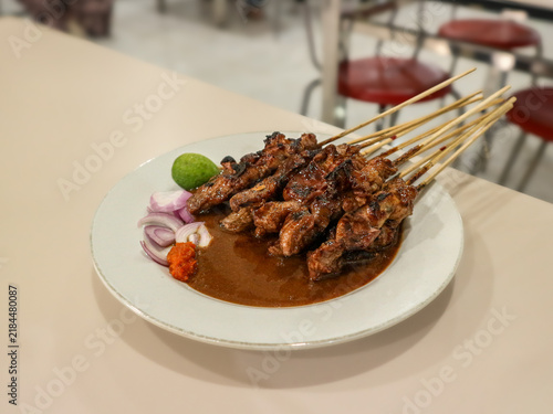 Obraz na plátně A plate of Indonesian-style sate kambing (goat meat satay) served with rich peanut sauce and accompanied by lime wedges, sliced shallots, and spicy sambal