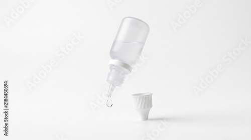 A small translucent plastic dropper bottle dispensing a single liquid drop against a white background with squeeze bottle releases nozzle above removed single clear