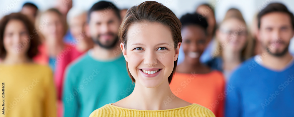 Fototapeta premium Smiling woman standing before diverse group portrait with confident expression and colorful clothing in bright studio setting
