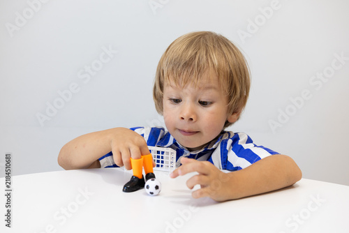 A boy plays finger football. A fair-haired child plays with a toy with small shoes and a ball. A model of a football for a children's game.