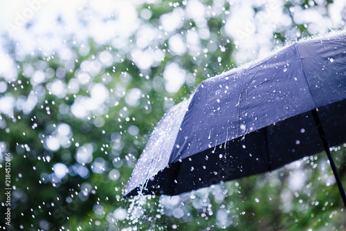 Black umbrella under rain against water drops splash background. Rainy weather concept.