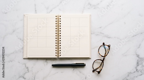 Open Planner with Glasses and Pen: An empty planner lies open, ready for notes and schedules, accompanied by reading glasses and a sleek pen, all set against a sophisticated marble surface.