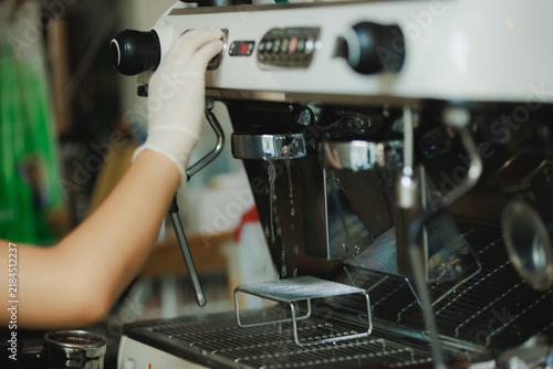 Close-up of a barista wearing white gloves flushing hot water through the group head of an espresso machine for cleaning and brewing prep at a cafe.